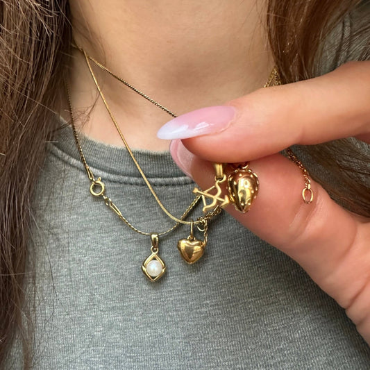 three necklaces worn on girl with green t-shirt, close up, bow and arrow charm, strawberry necklace, heart of gold necklace ani pear charm necklace