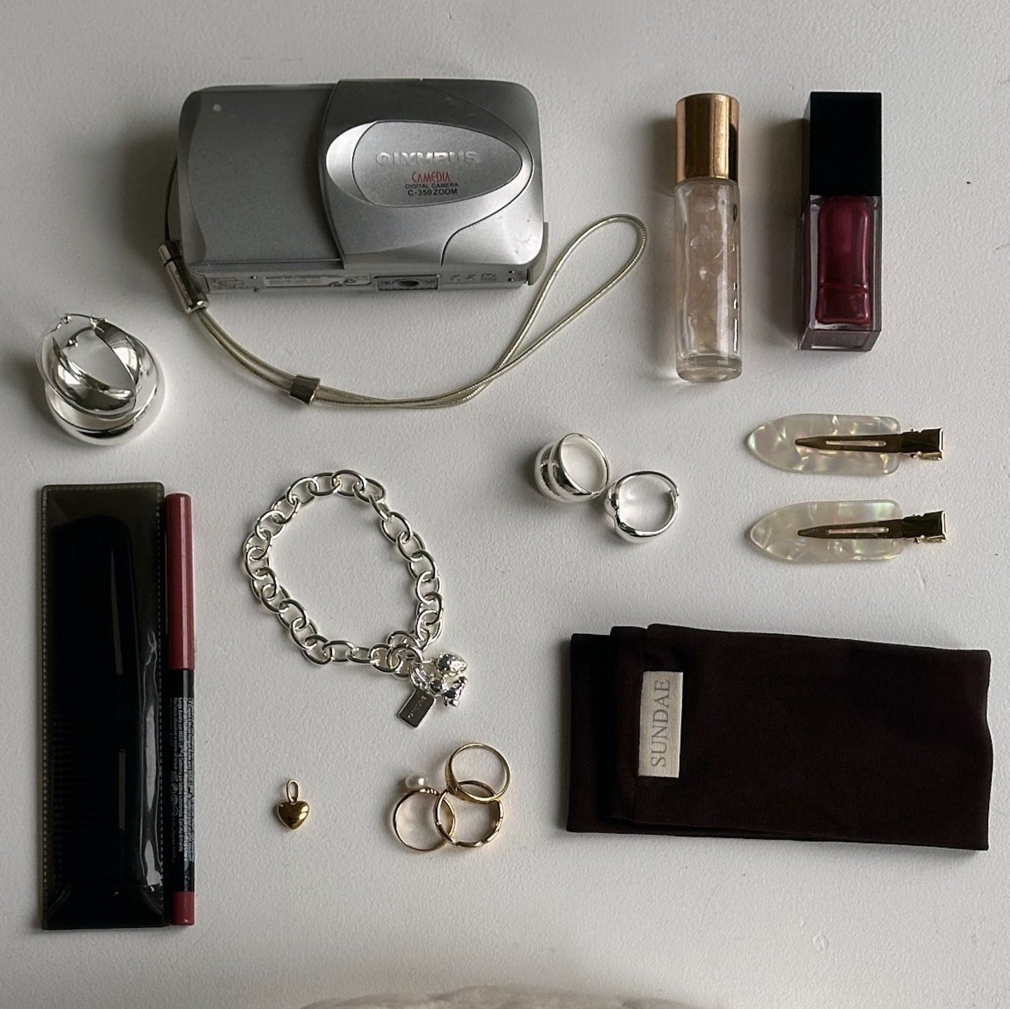 Konstellation von Kamera, Lipgloss, Make-up und Haarprodukten auf weißem Schreibtisch mit Schmuckstücken in Silber