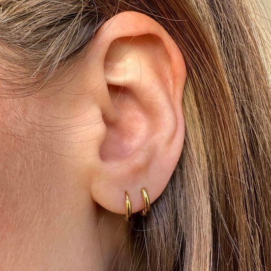 Mini Creolen in gold getragen im ersten und zweiten Ohrloch einer Frau