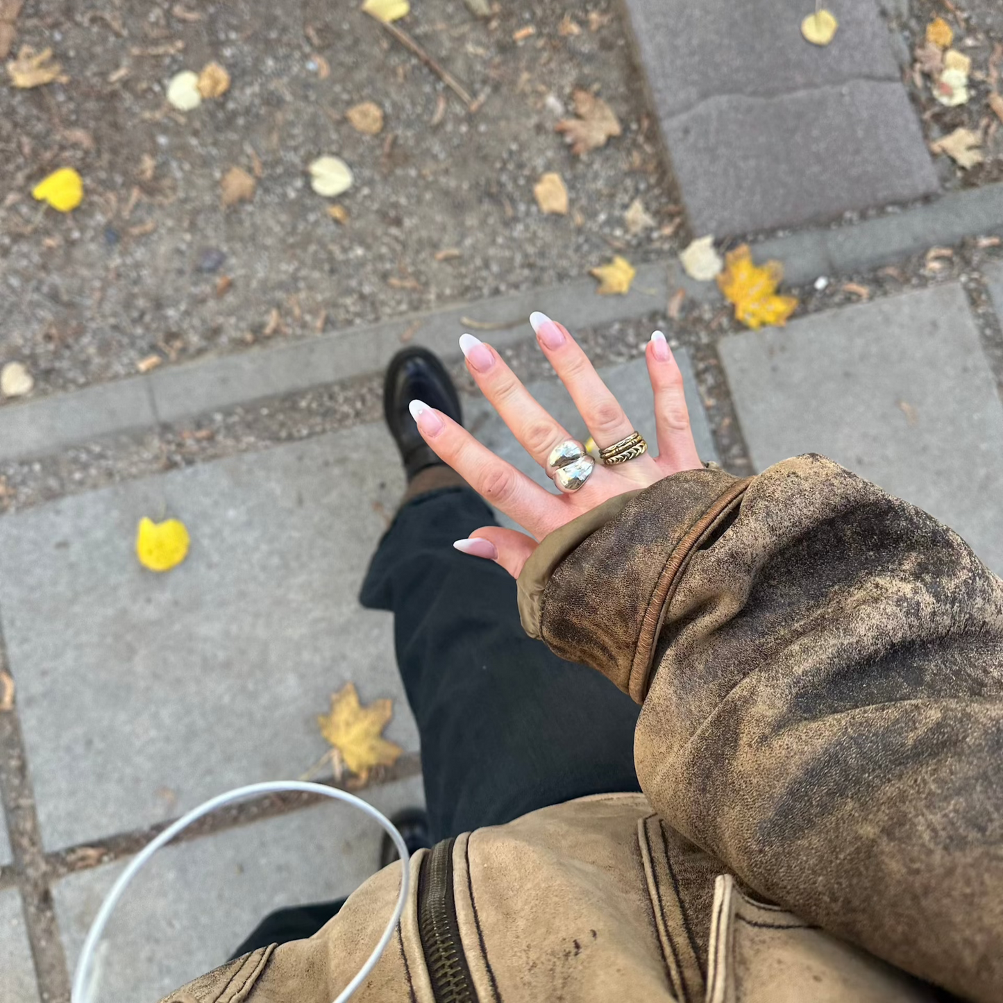 Kräftiger Schmuckring und Goldringstapel, der in der Hand getragen wird, während man mit gelben Blättern auf dem Boden durch die Straßen geht