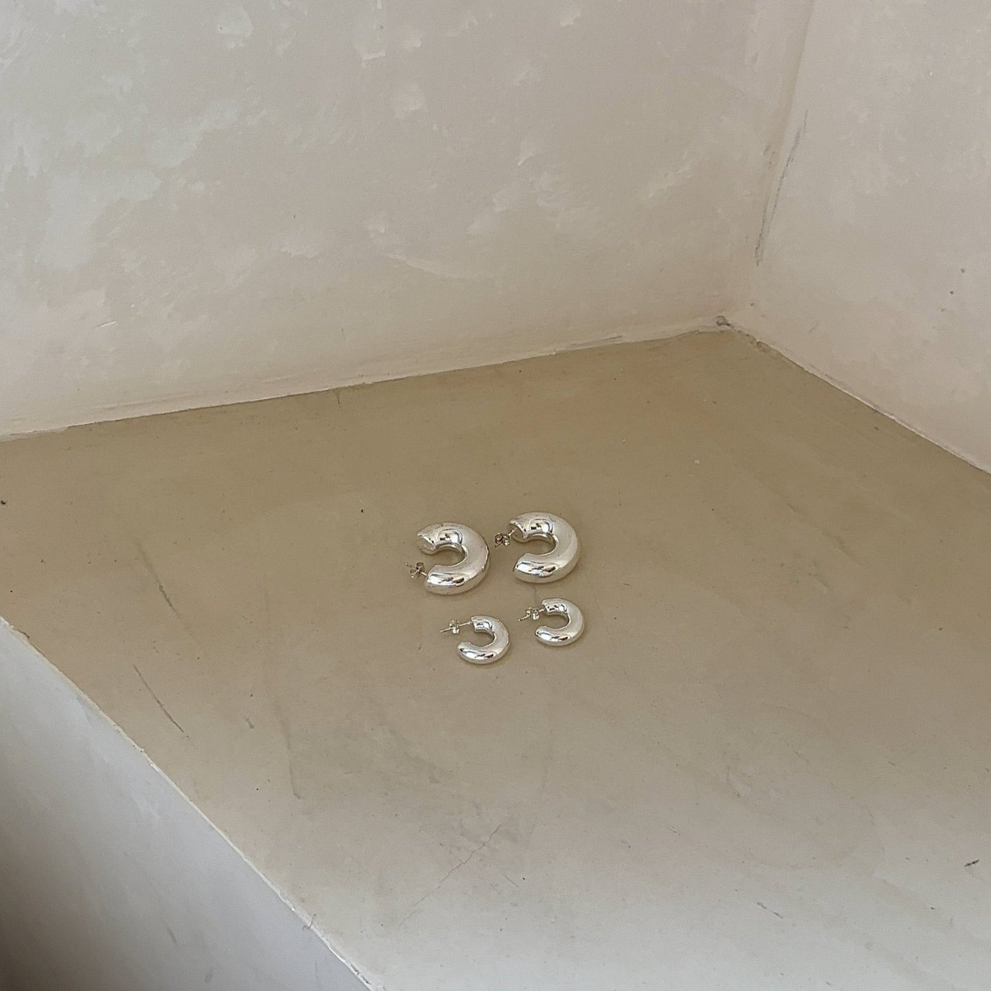 Silber Ohrring Creolen in groß und klein auf beige Ecke des Raumes
