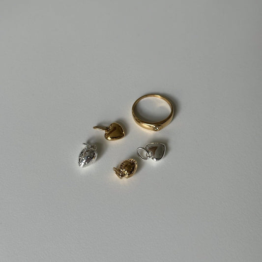 gigi ring and heart and strawnberry charm in silver and gold on white table
