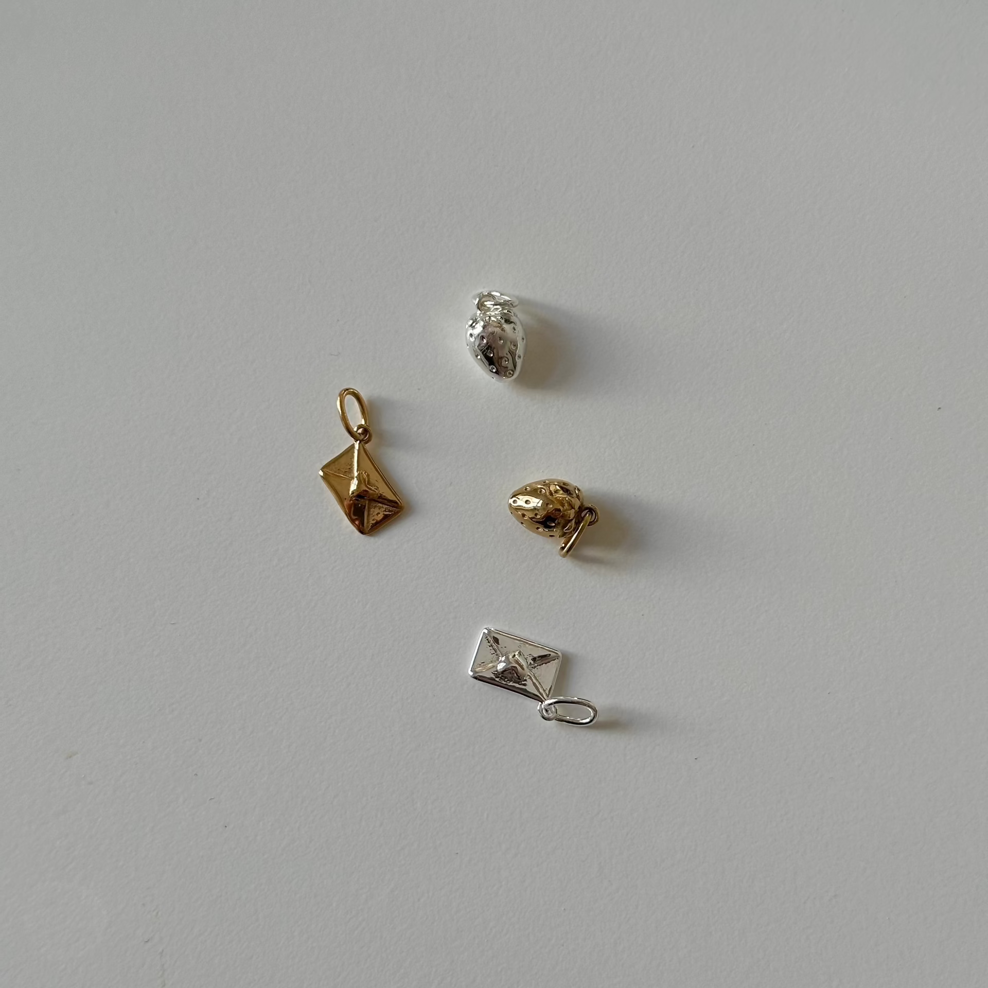 love letter and strawberry charm in silver and gold on white table 